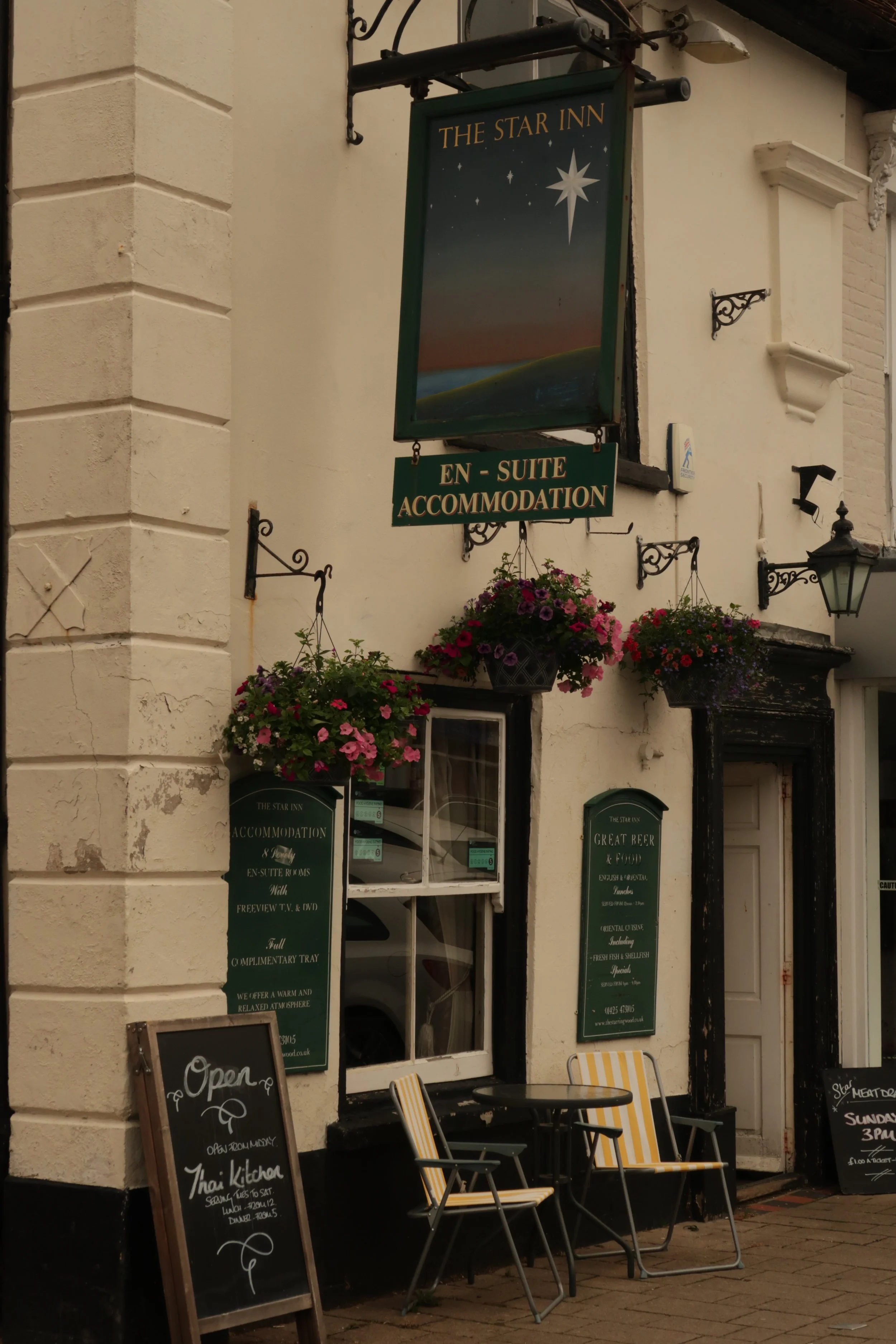 The exterior of a pub or restaurant called The Star Inn, featuring hanging flower baskets, chalkboard signs advertising Thai cuisine and music events, outdoor tables and chairs, and signage mentioning en-suite accommodation and various amenities, wit