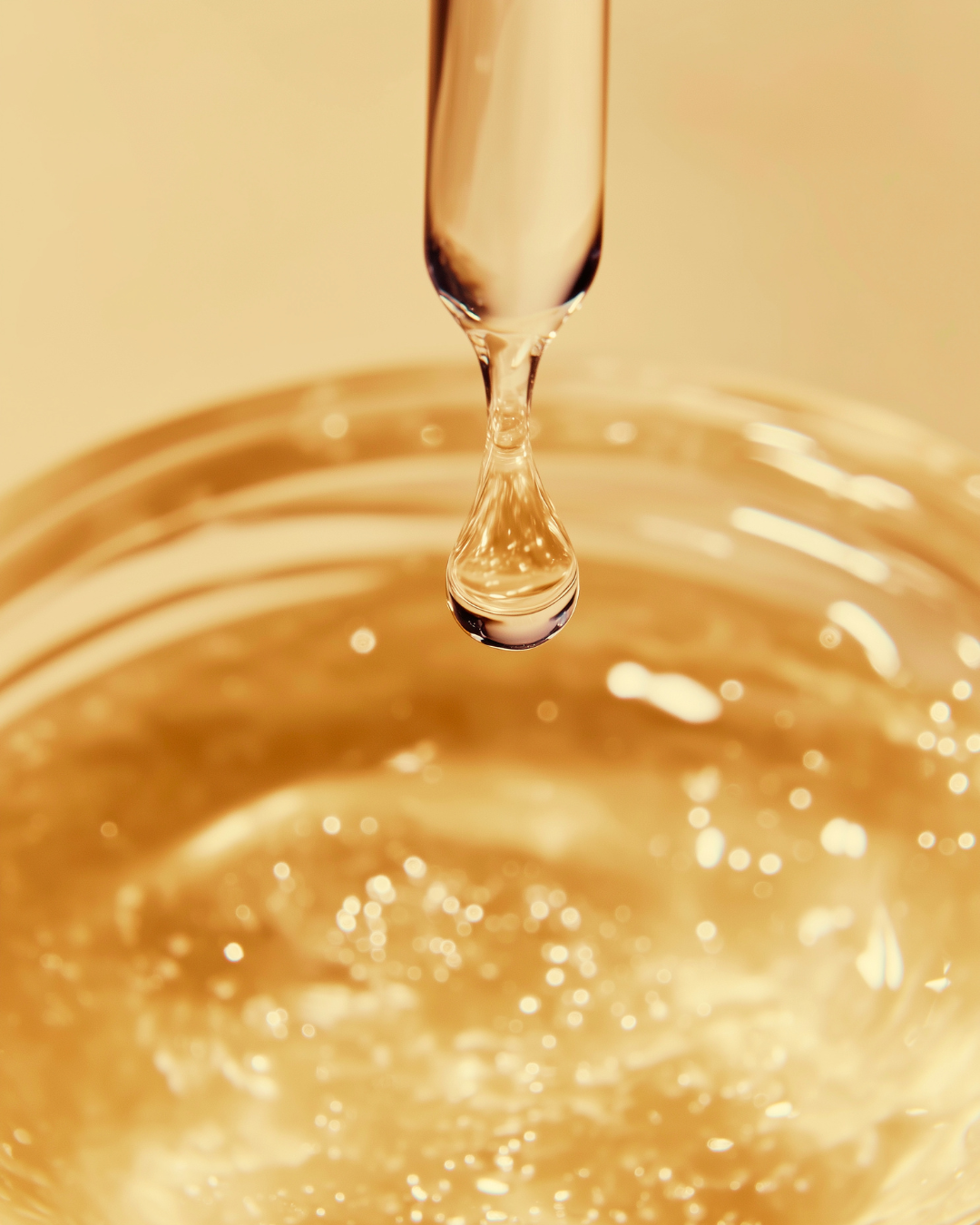 Close-up of a golden liquid, with a droplet falling from a pipette into a glass of sparkling gold-colored skincare serum