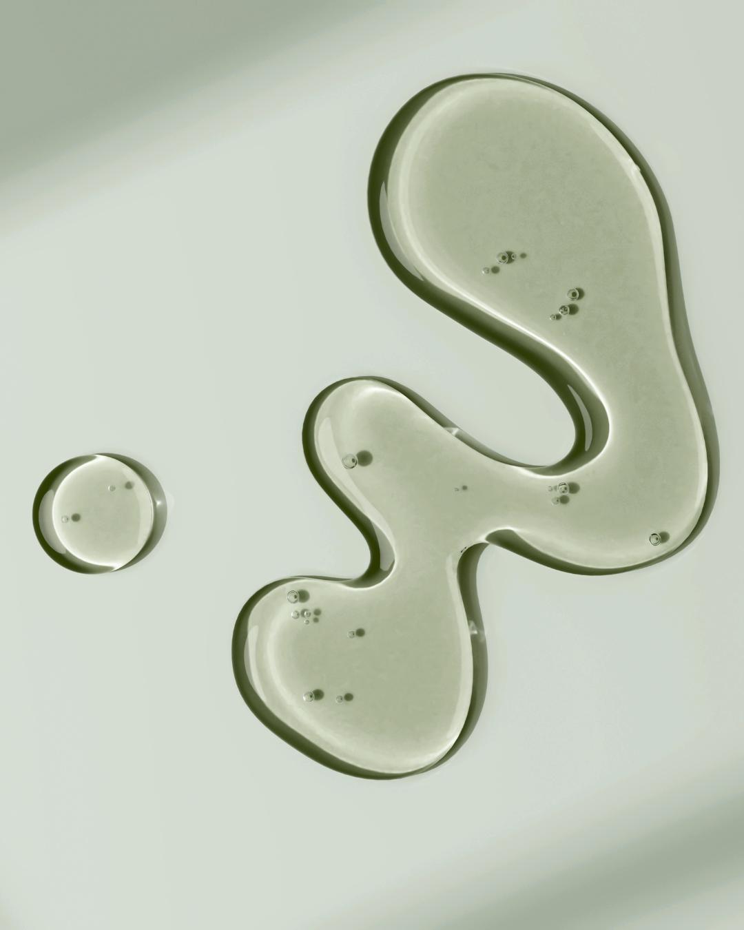 Close-up of a few drops of oil or liquid on a pale background, green translucent skin serums.