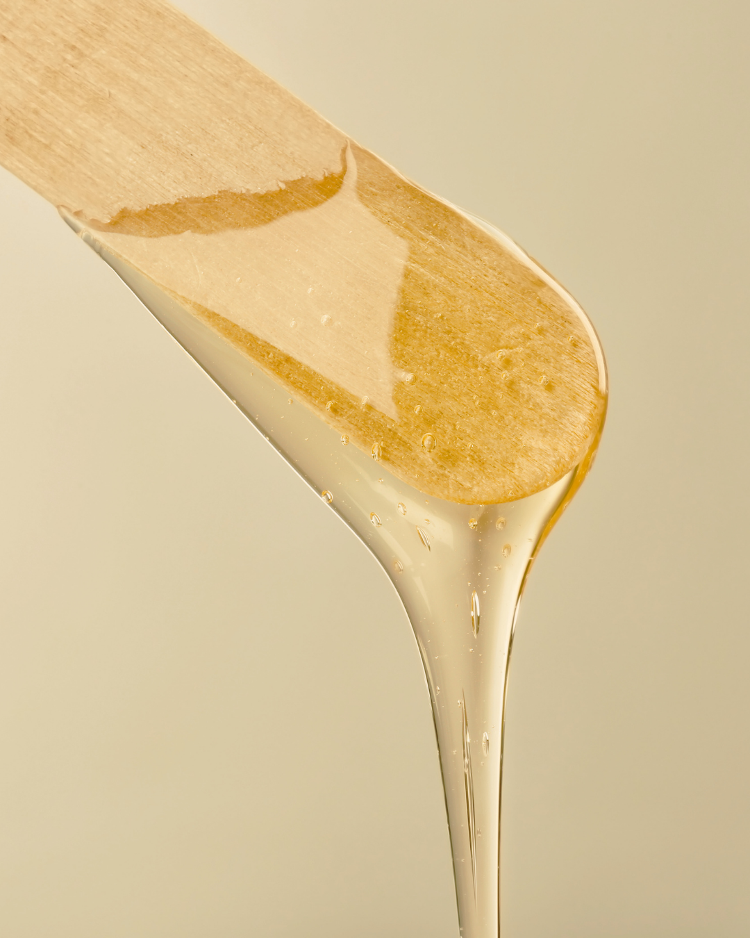 Close-up of a wooden spatula with melted waxing wax dripping from its edge.