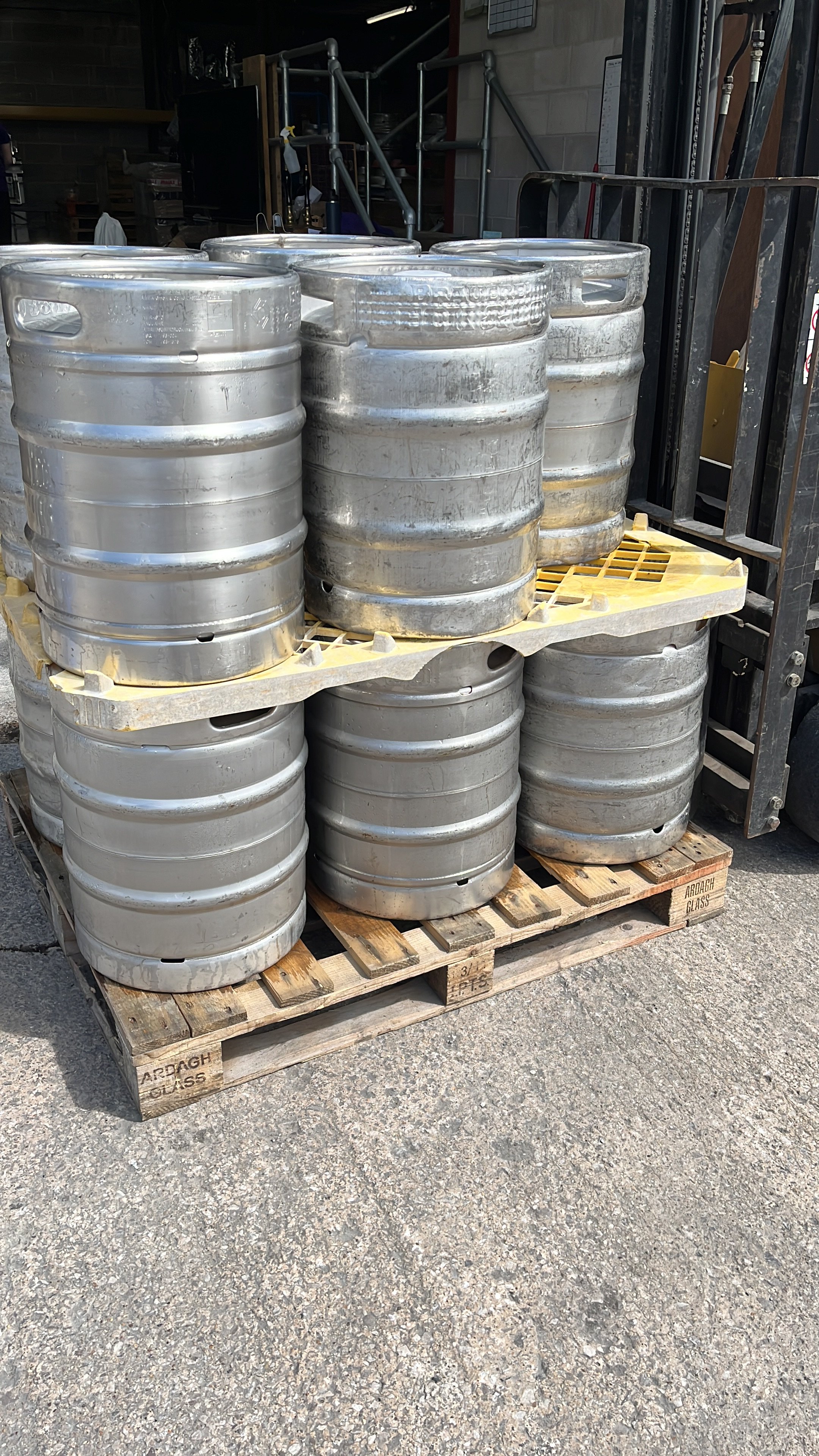 Pallet of stainless steel beer kegs stacked outside on concrete pavement.