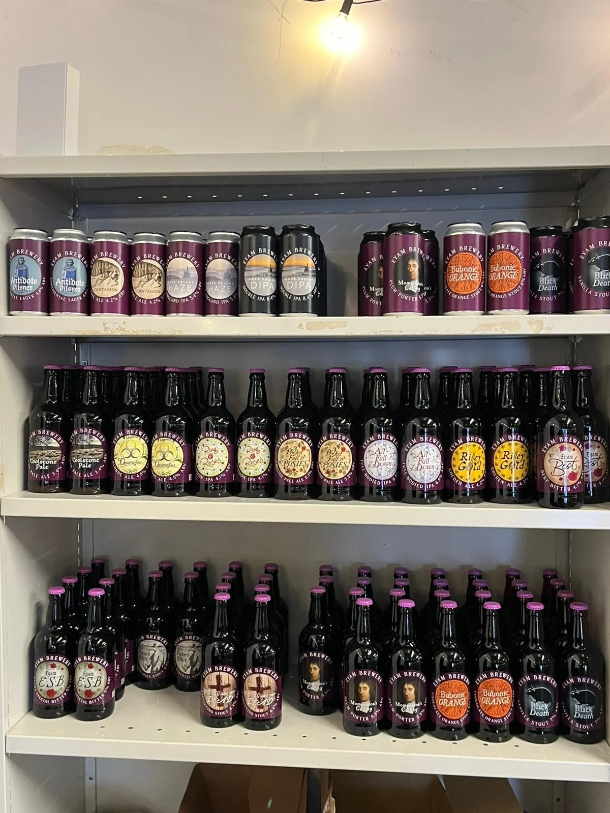 Shelf of craft beer bottles and cans with purple, black, and white labels, featuring various brewing styles and flavors.