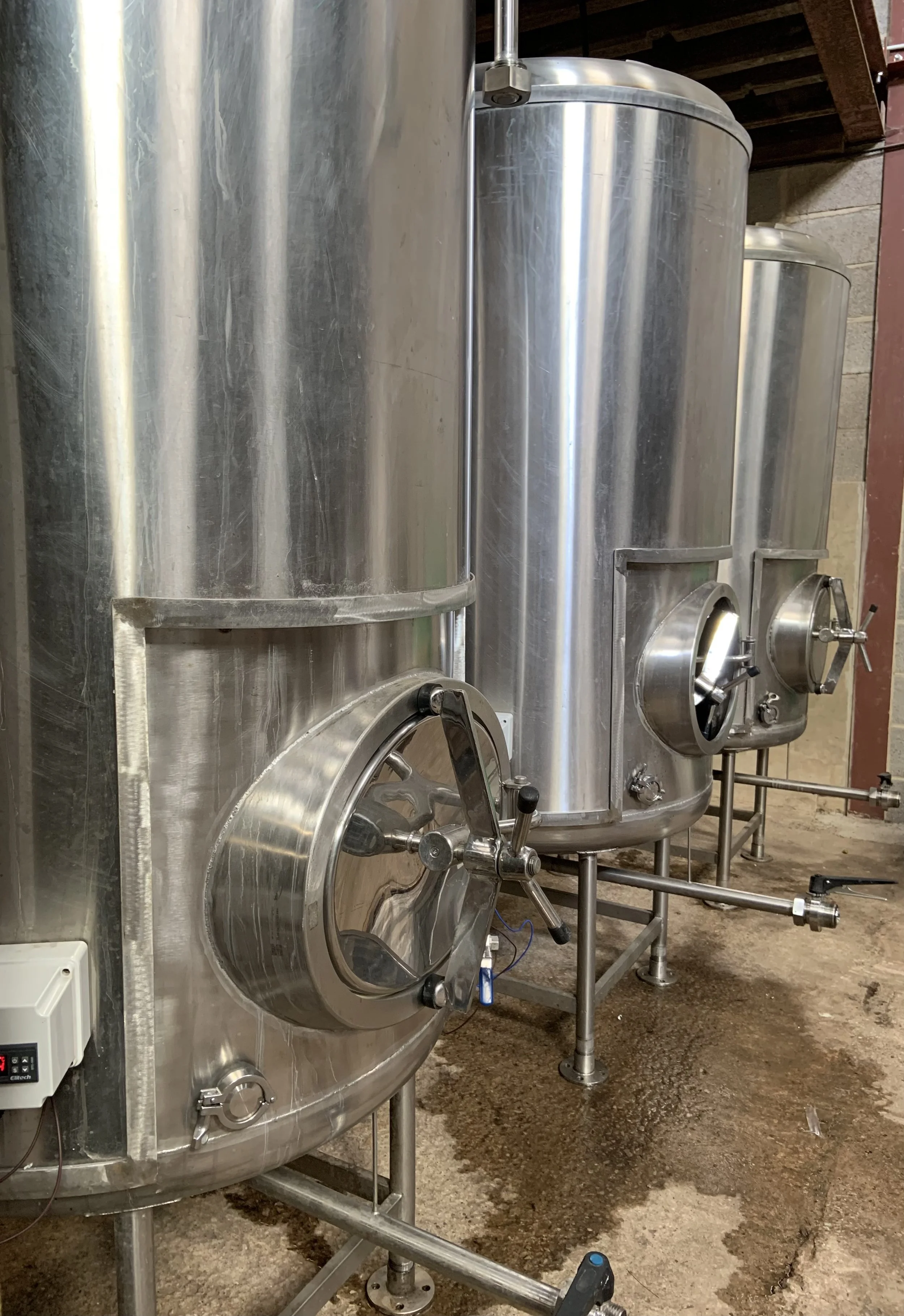 Three large cylindrical stainless steel tanks in a brewery or industrial setting.