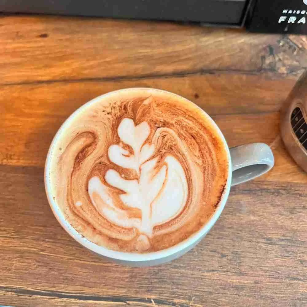 A cup of coffee with latte art in the shape of a leaf on top, sitting on a wooden surface in a cafe in Morecambe