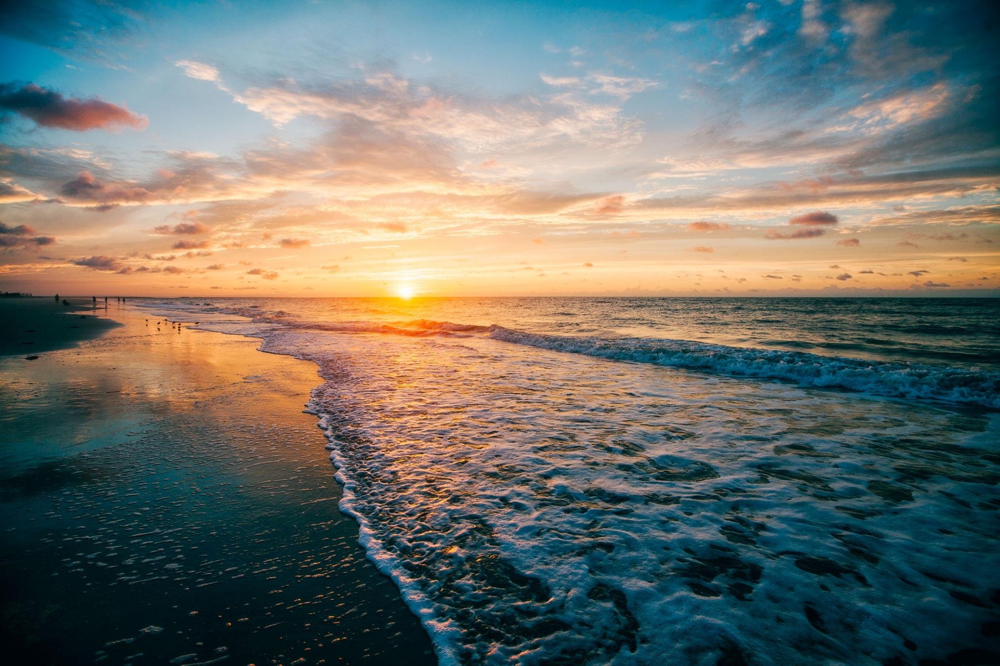 Sunset over the ocean with waves and a colorful sky with clouds.