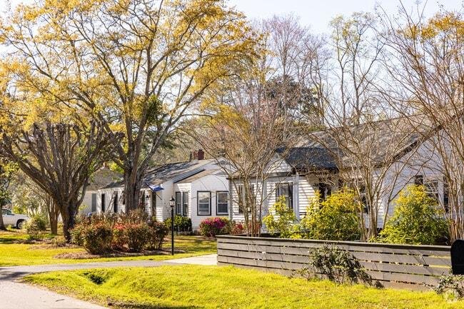 Suburban neighborhood with single-story white house, trees with yellow and brown leaves, green lawn, and a wooden fence.