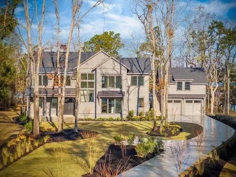 Large modern house surrounded by trees and a well-maintained lawn with a driveway.