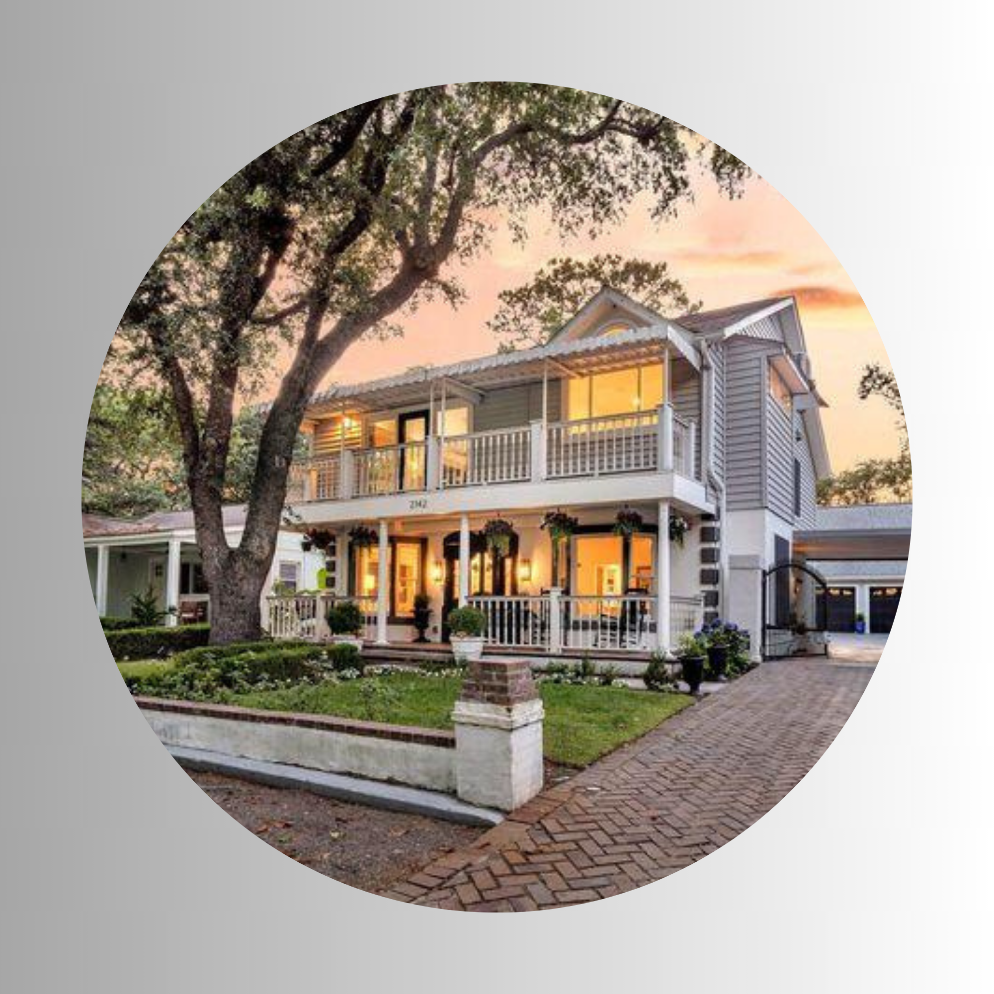 A two-story house with a porch and balcony, grey siding, and white trim, surrounded by trees, at sunset with a pink sky.