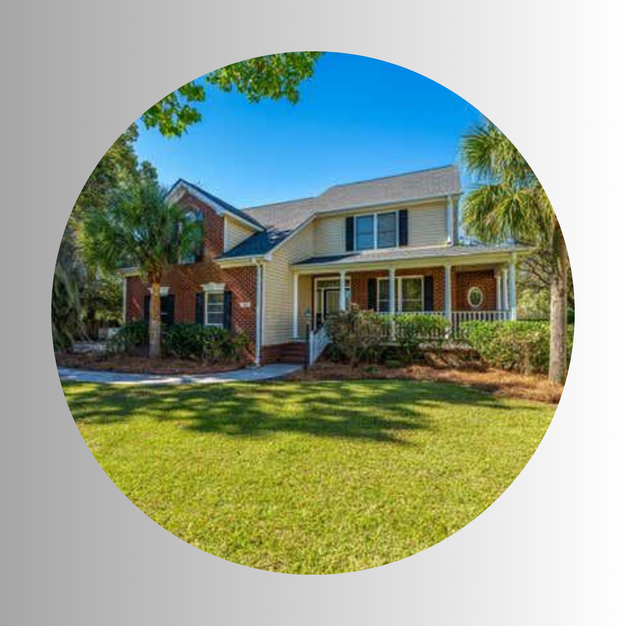 A two-story house with beige siding, brick accents, and a gray shingle roof, surrounded by trees and a well-manicured lawn under a clear blue sky.