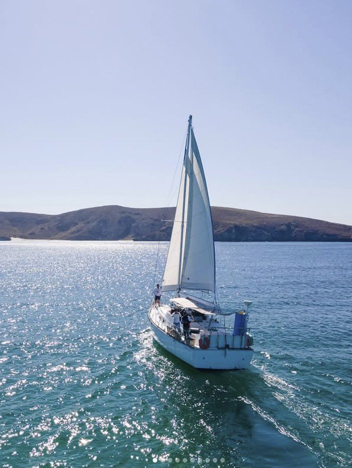 Velero navegando en aguas abiertas con colinas en el horizonte bajo cielo despejado.