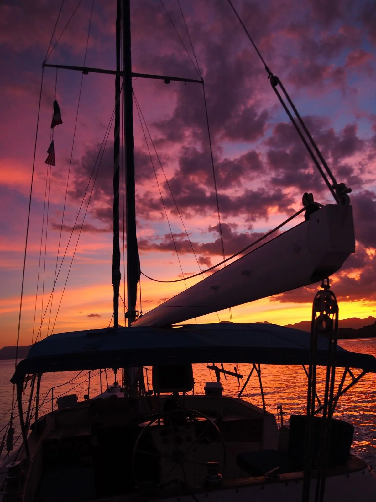 Velero en el agua durante un atardecer con cielo colorido de tonos rosados, morados y naranjas.