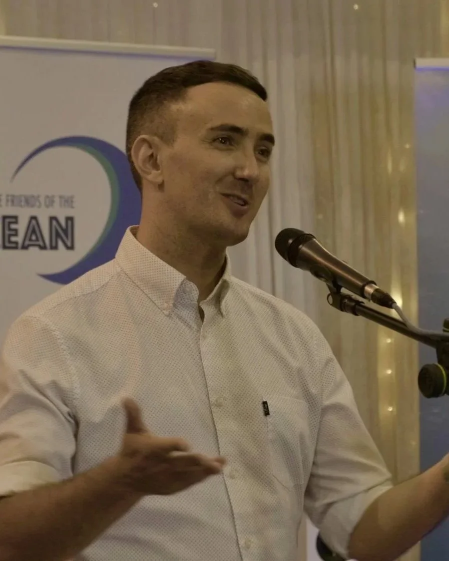 A man speaking at a microphone during a presentation at an event. There is a banner in the background with the words 'Friends of the Ocean".