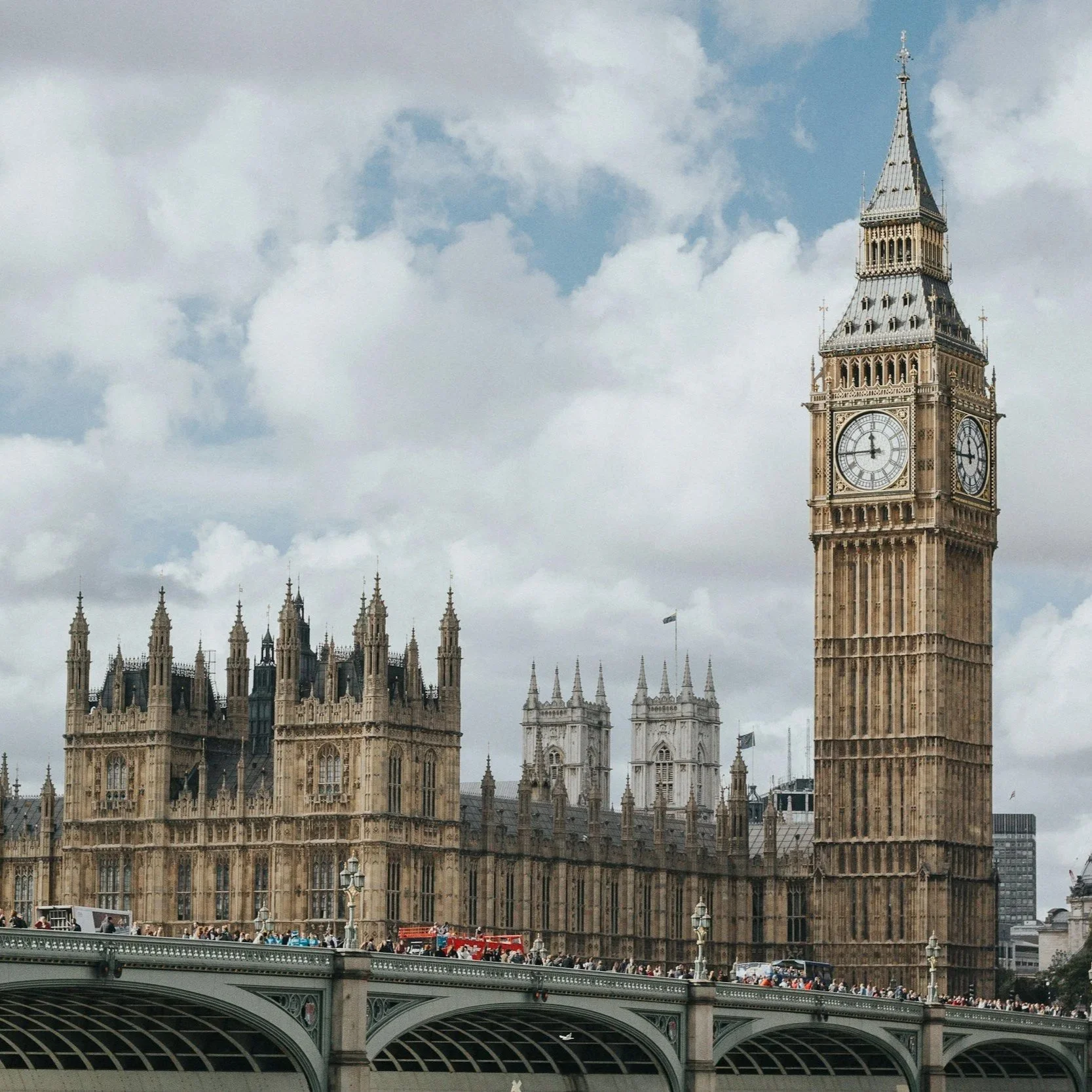 Big Ben clock tower and the Houses of Parliament in London, England, with a cloudy sky and a river with a bridge in the foreground.