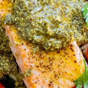 Close-up of seasoned cooked salmon topped with green pesto sauce and garnished with fresh herbs.