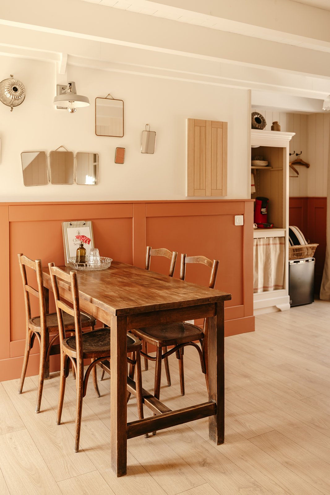 Intérieur de la chambre Dulse au Clos des Sentiles avec une table en bois et quatre chaises, des murs décorés avec plusieurs petits miroirs de barbier et un coin café aménagé dans un ancien meuble.