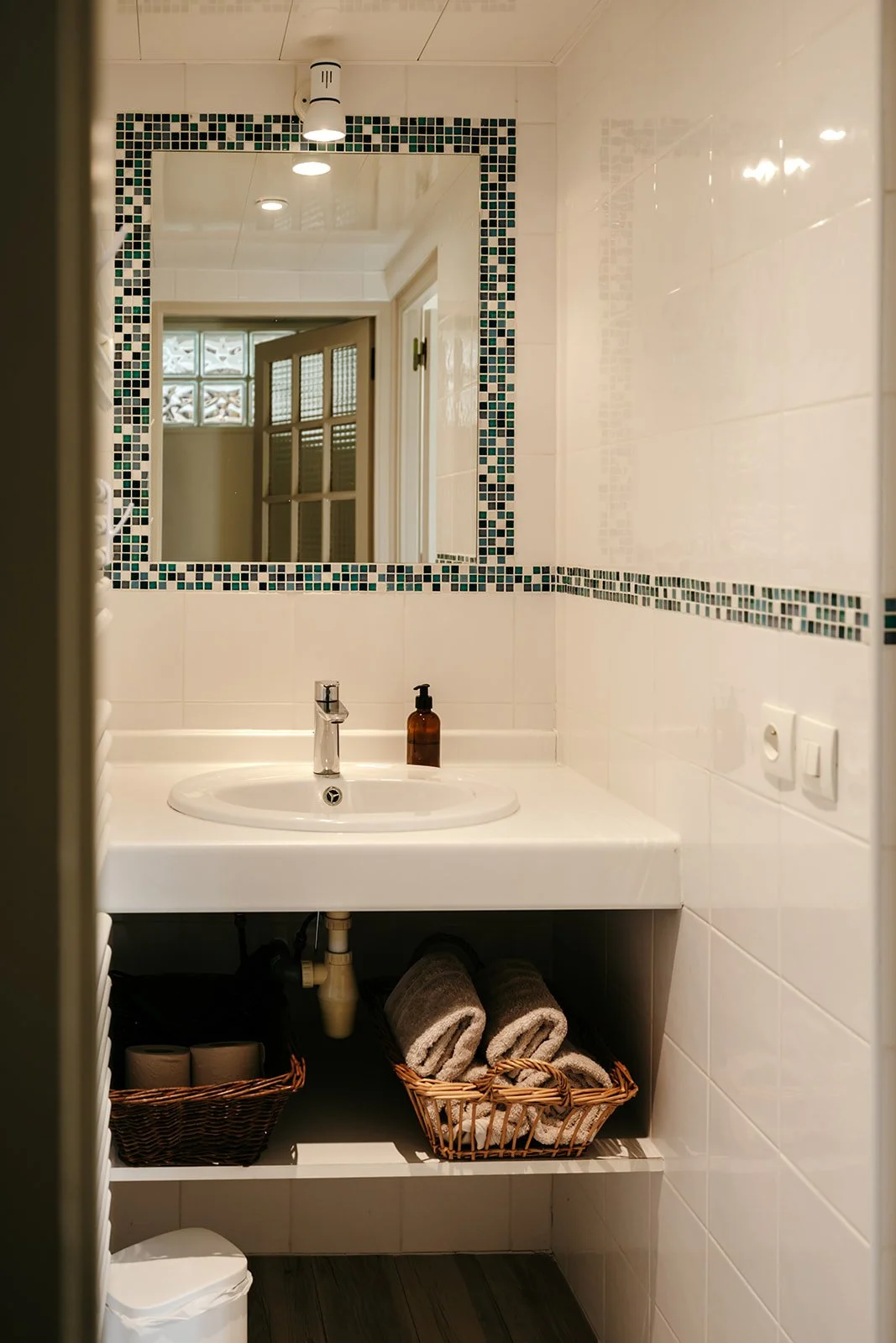 Petite salle de bain avec un miroir, un lavabo, un savon liquide, des serviettes dans une corbeille, et un miroir mural