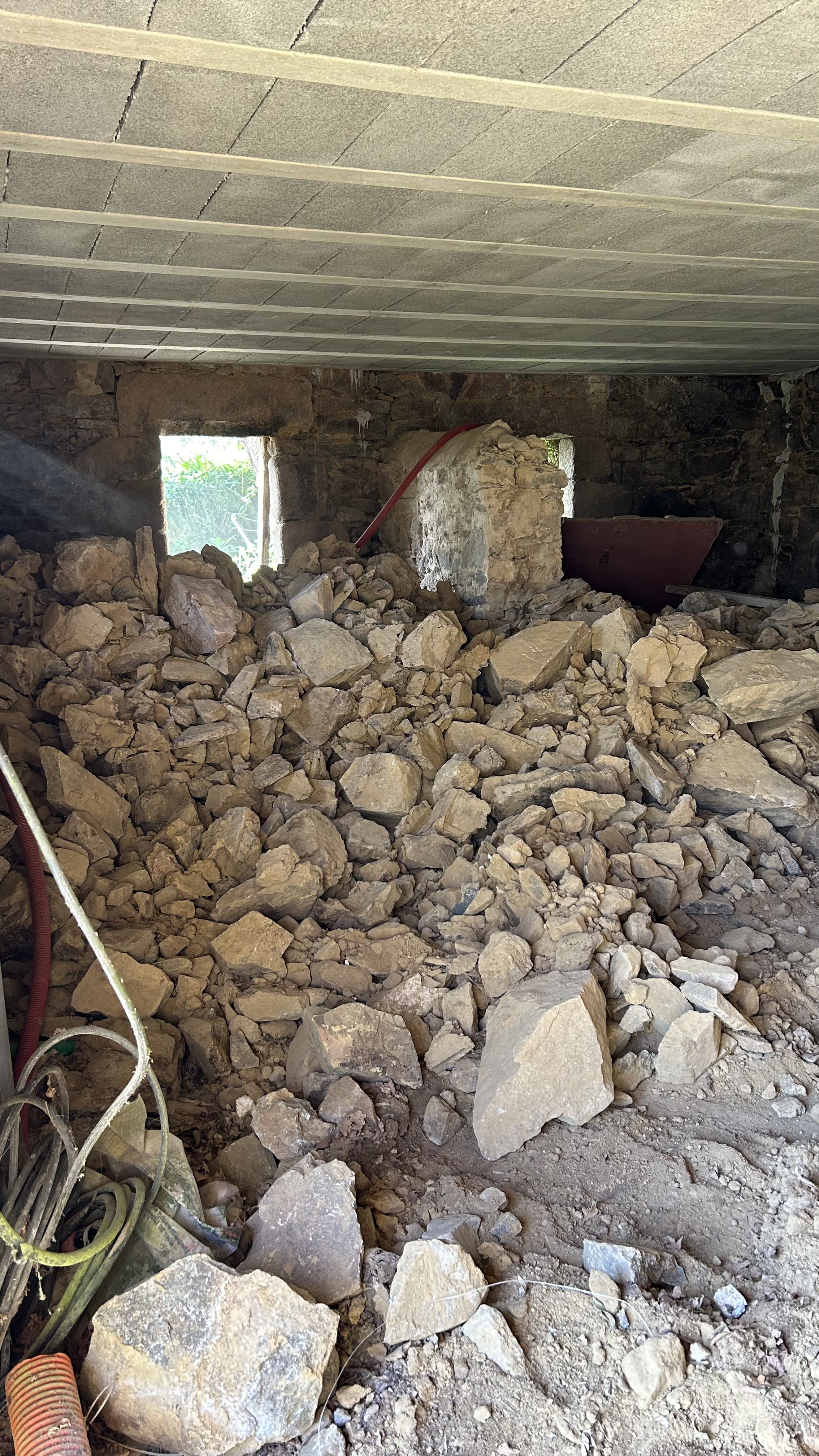 Intérieur d'une construction avec un sol recouvert de débris en pierre, des murs en pierre et une ouverture laissant passer la lumière.