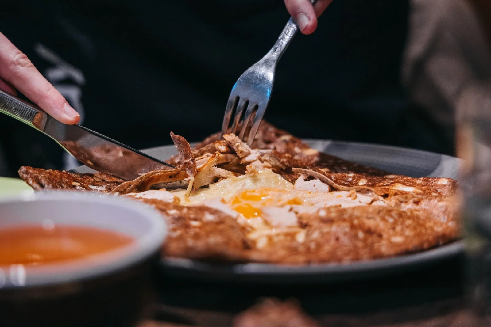 Une personne découpe une plat avec des morceaux de viande et un œuf au plat au centre.