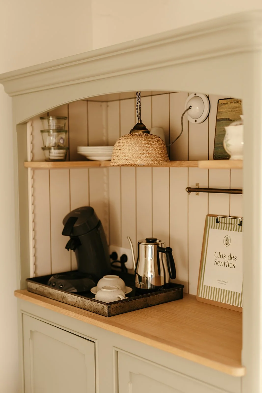Coin café avec machine à café, bouilloire électrique, tasses et le livre d'accueil de la chambre d'hôtes 'Clos des Sentiles' dans un décor de cuisine rustique.