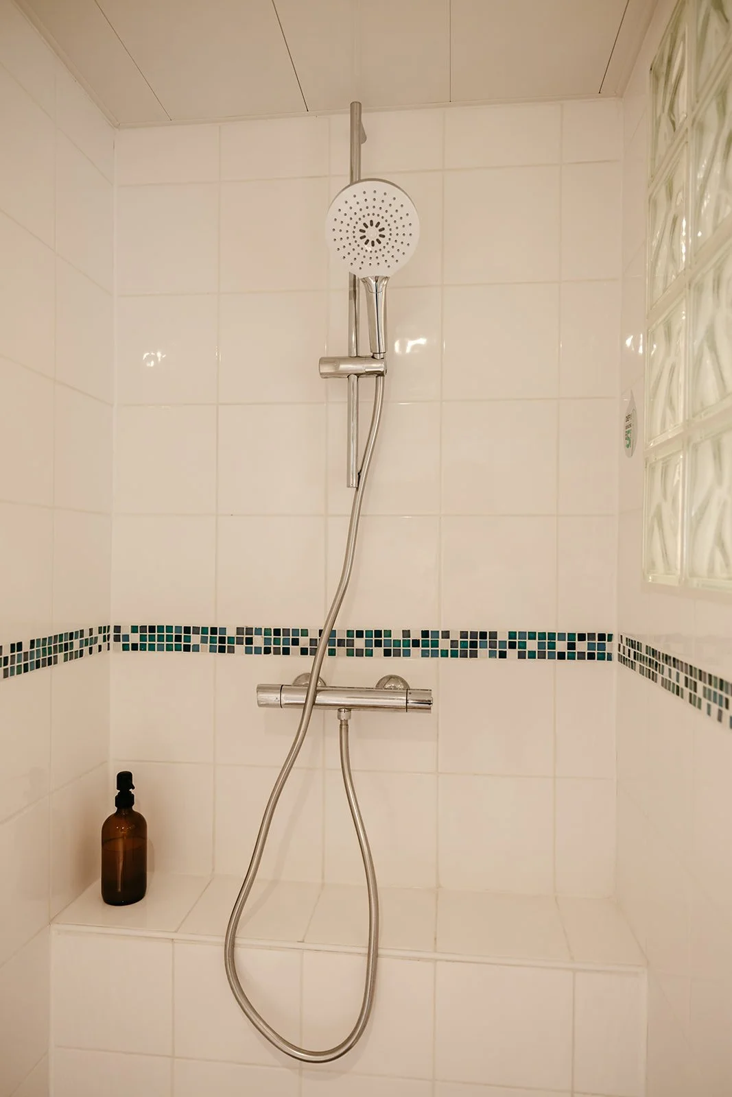 Douche italienne avec un mur en céramique blanc, une bouteille en verre ambré face gel douche et un mitigeur.