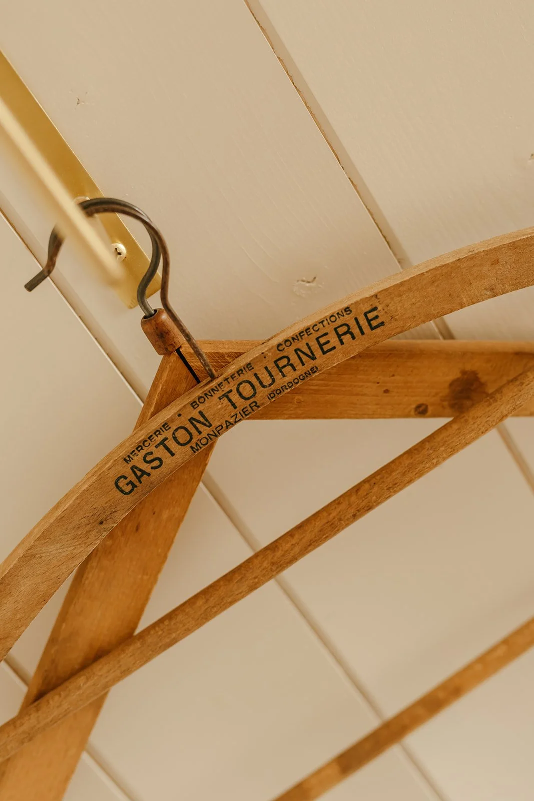 Un cintre en bois avec l'inscription 'Gaston Tournerie', suspendu à un crochet en laiton.