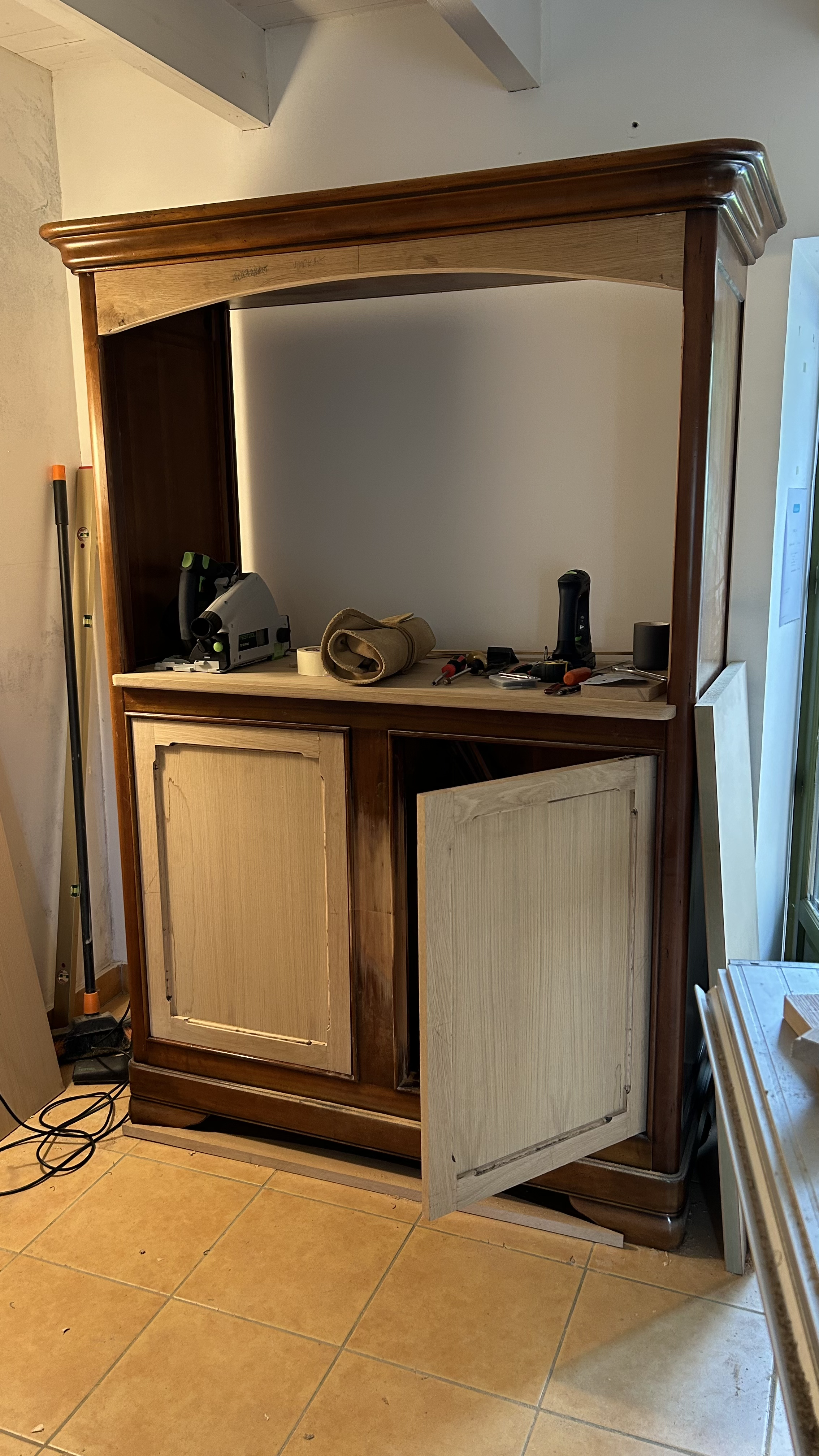 Un meuble en bois en cours de rénovation avec des outils posés dessus, portes partiellement ouvertes, dans une pièce de maison.