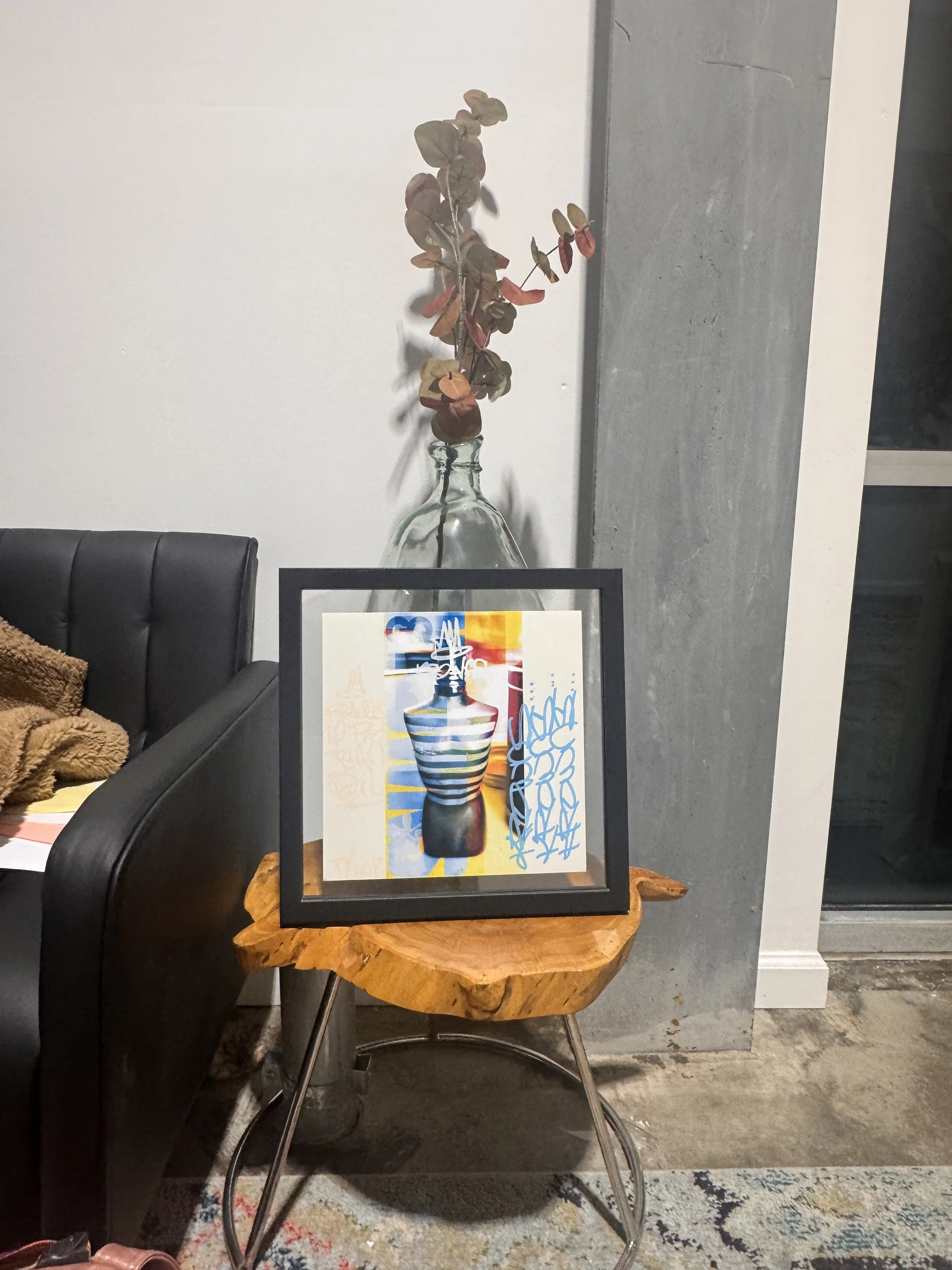 A framed modern art print of a colorful, abstract vase with abstract lines and shapes, placed on a rustic wooden table.