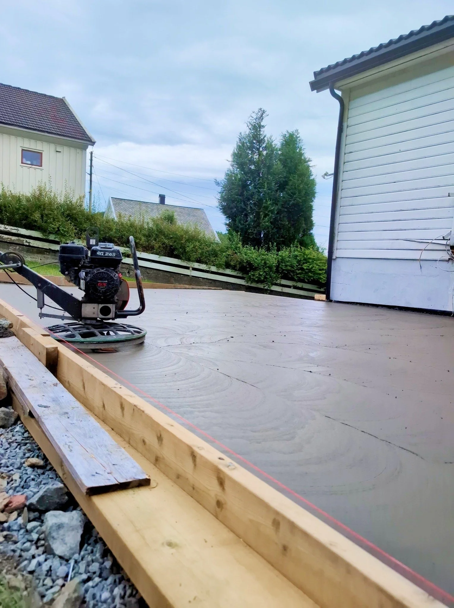 Bilde av en ferdig betongplate med tilstøtende treverk og en motsatt hvit husvegg. I bakgrunnen ser man tre store trær og noen hus. Det er overskyet vær.