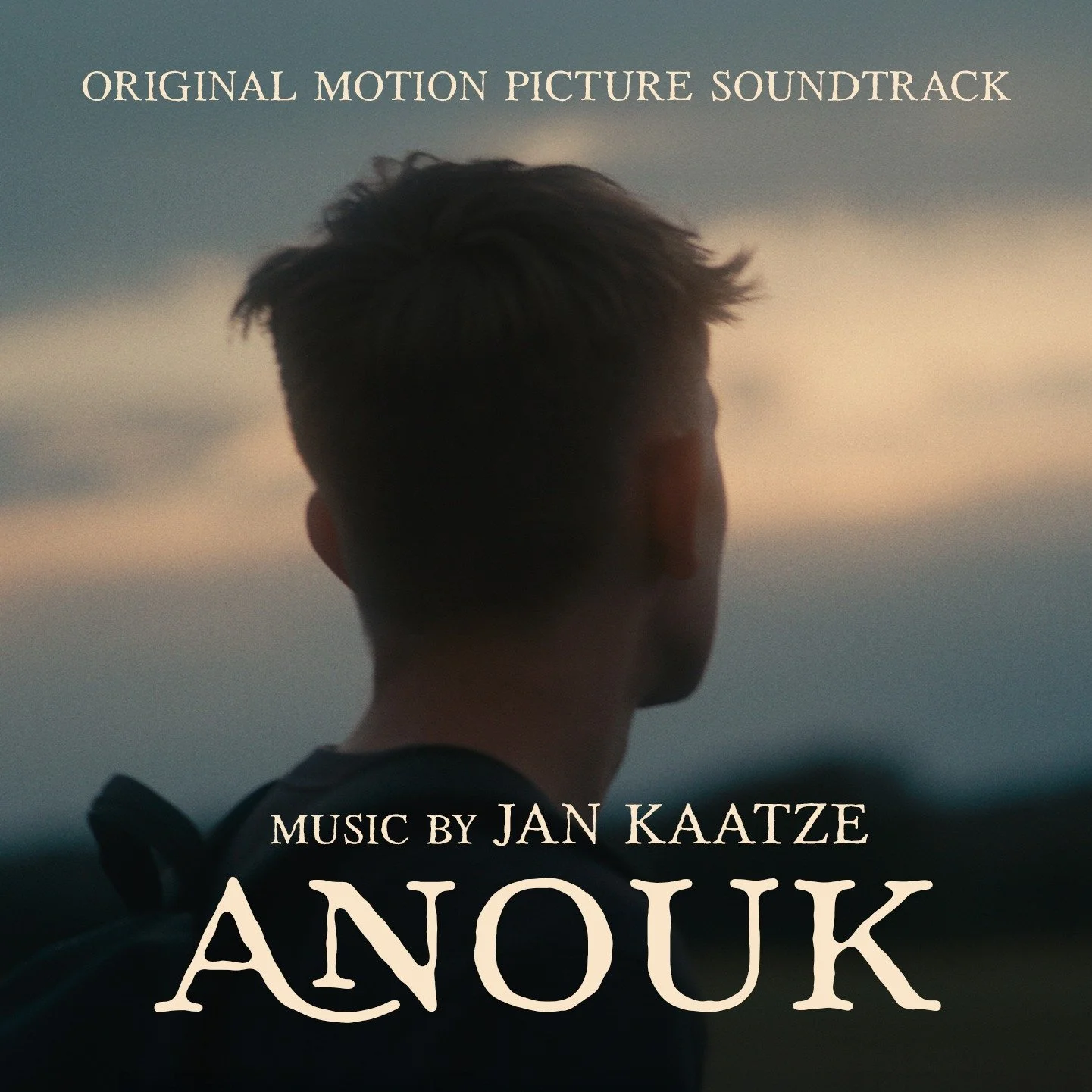 Back of person with dark hair, looking at sunset or sunrise sky with clouds, overlaid with text advertising a soundtrack and music by Jan Kaatze.