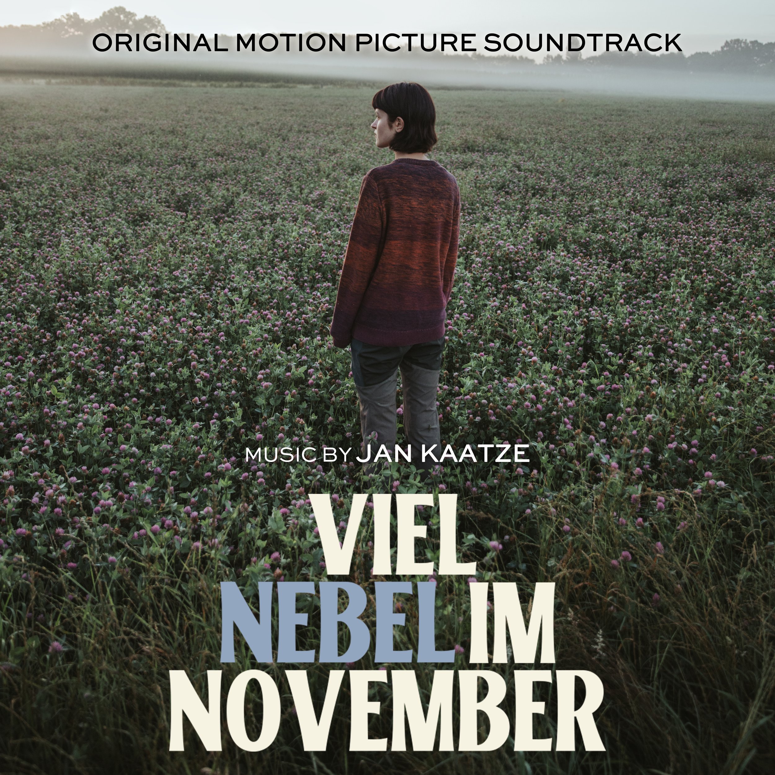 A person with short dark hair wearing a red and black sweater standing in a field of pink flowers with a foggy background, overlaid with text advertising a soundtrack and music by Jan Kaatze.