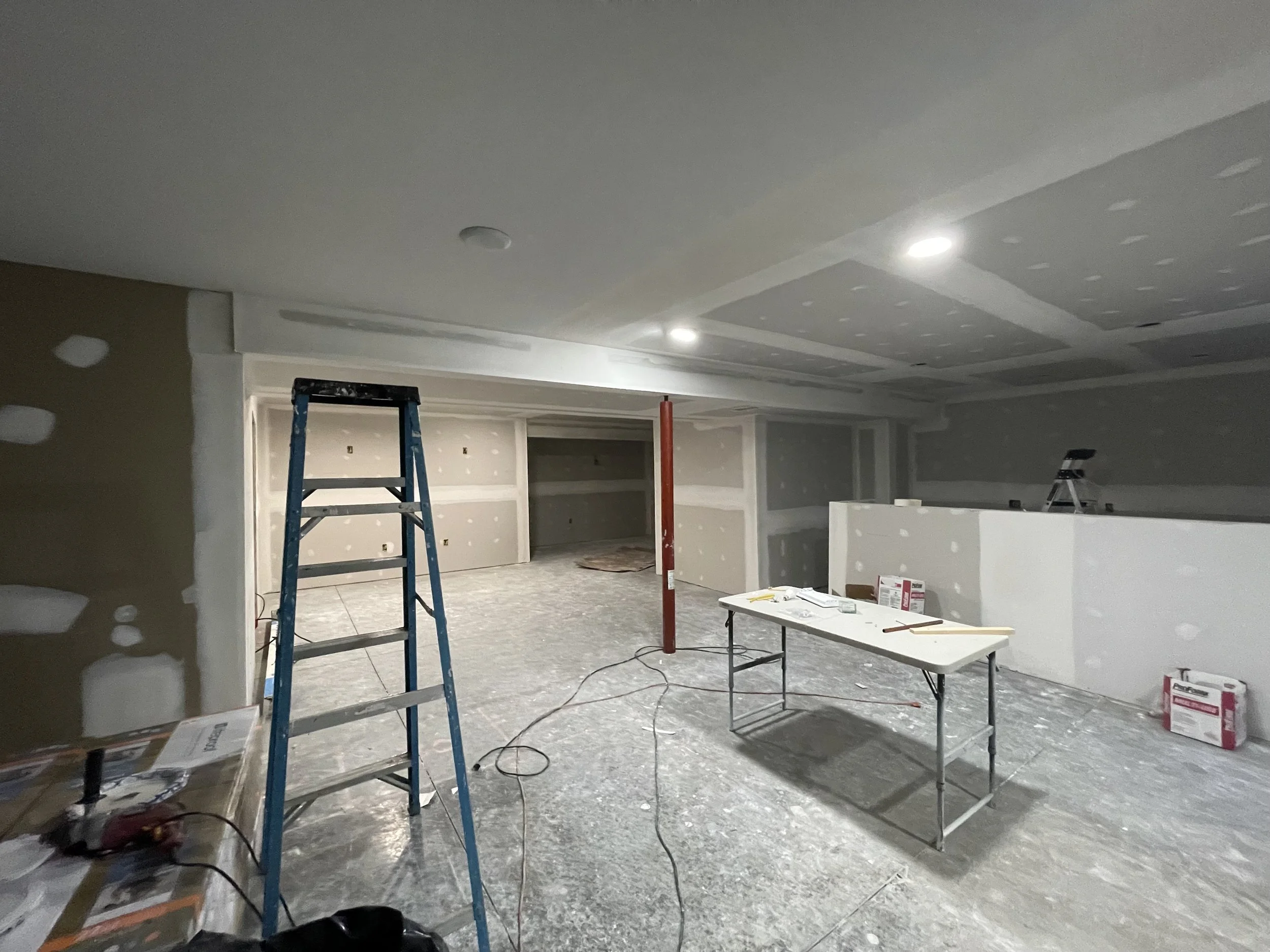 Interior of a room under construction, with unfinished drywall, construction tools, and scaffolding.