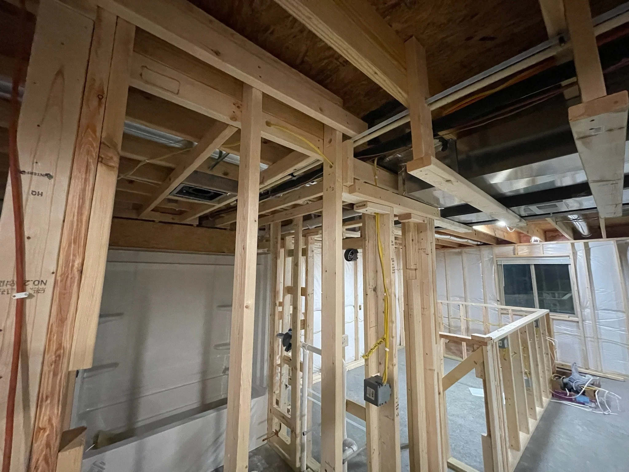 Wood framing for interior walls in a construction site, with electrical wiring and piping visible.