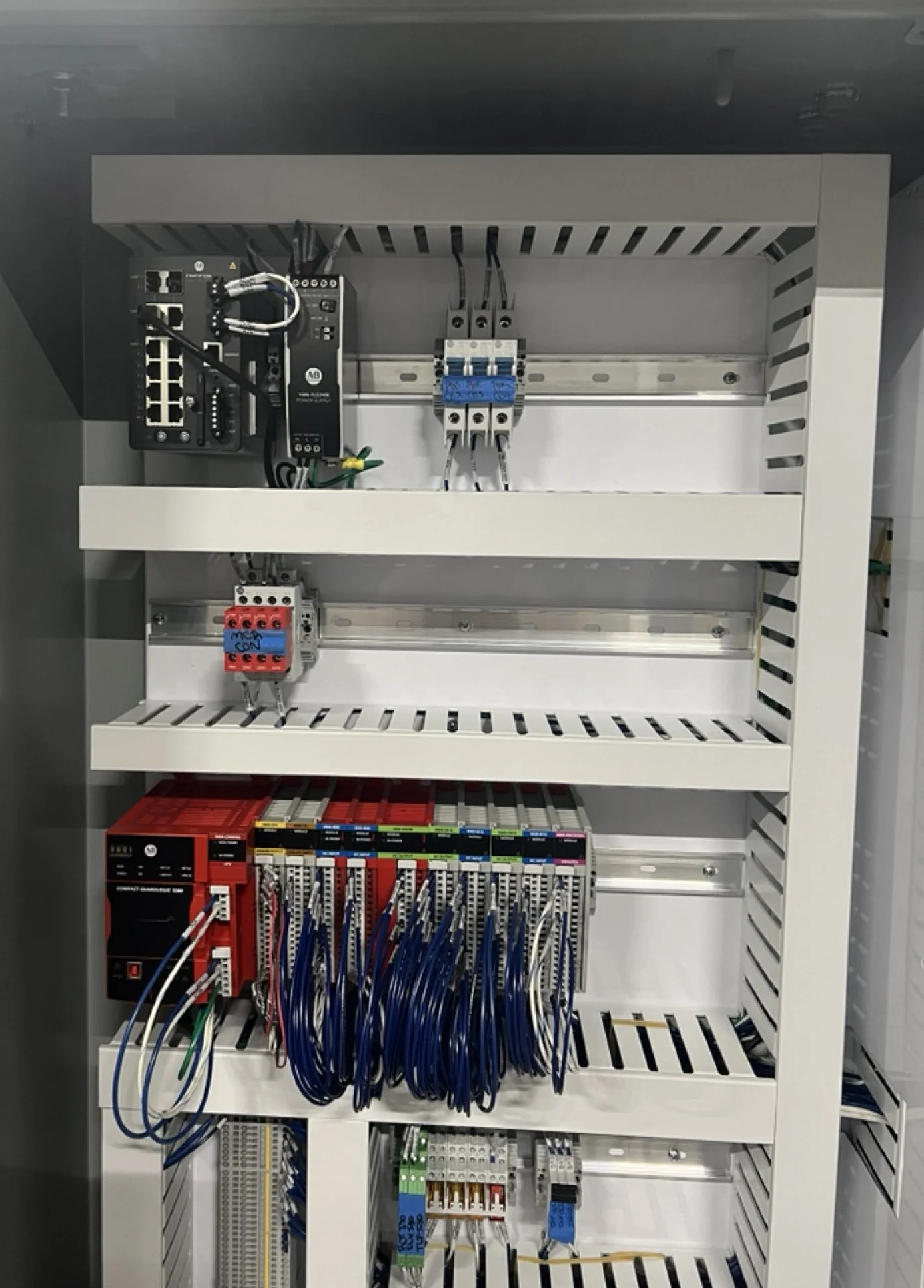 Electrical control panel with various wires, switches, and electrical components inside a white metal enclosure.