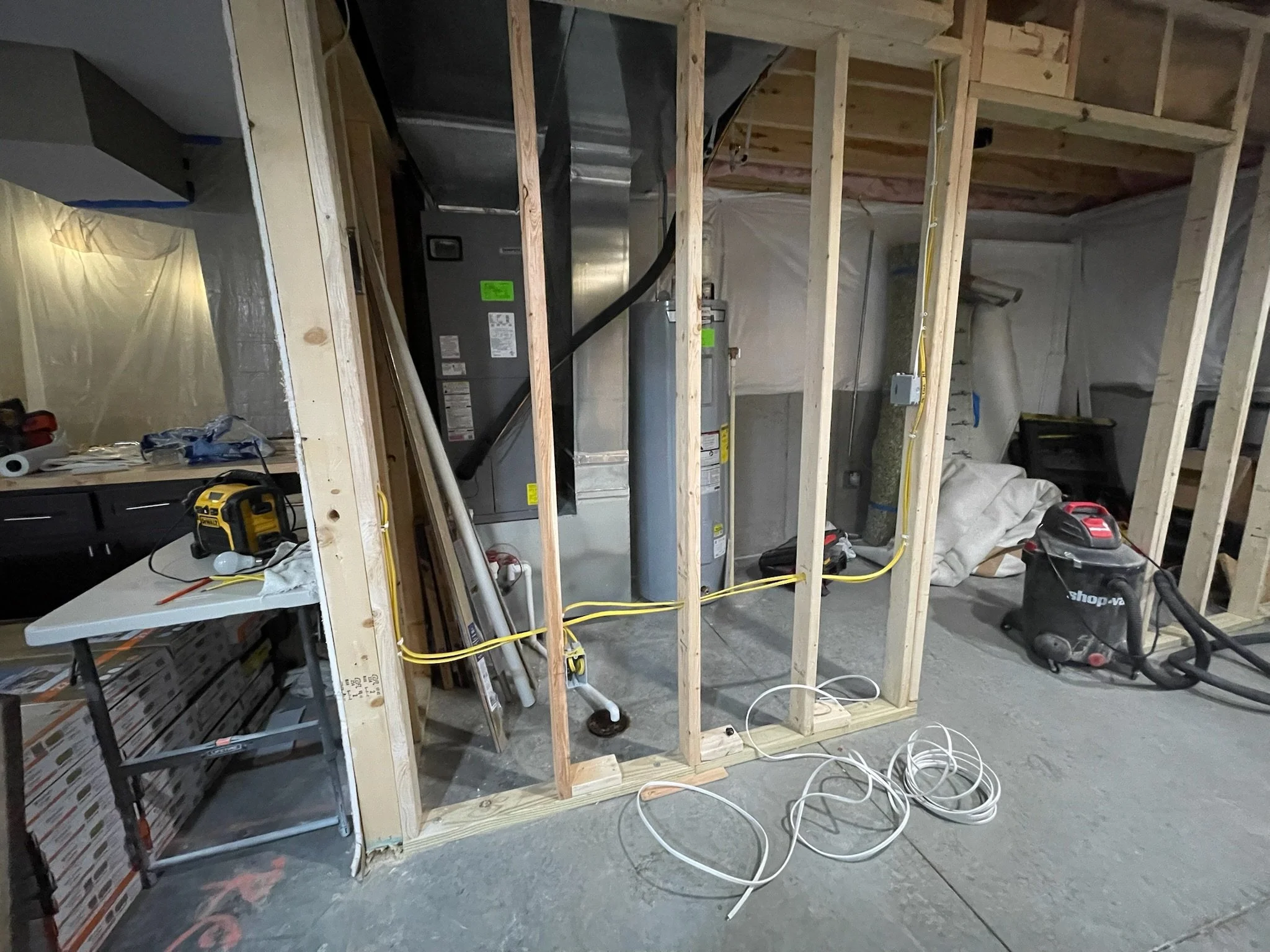 Interior of a building under construction with exposed wooden framing, electrical wiring, and HVAC equipment installed, with tools and materials scattered around.