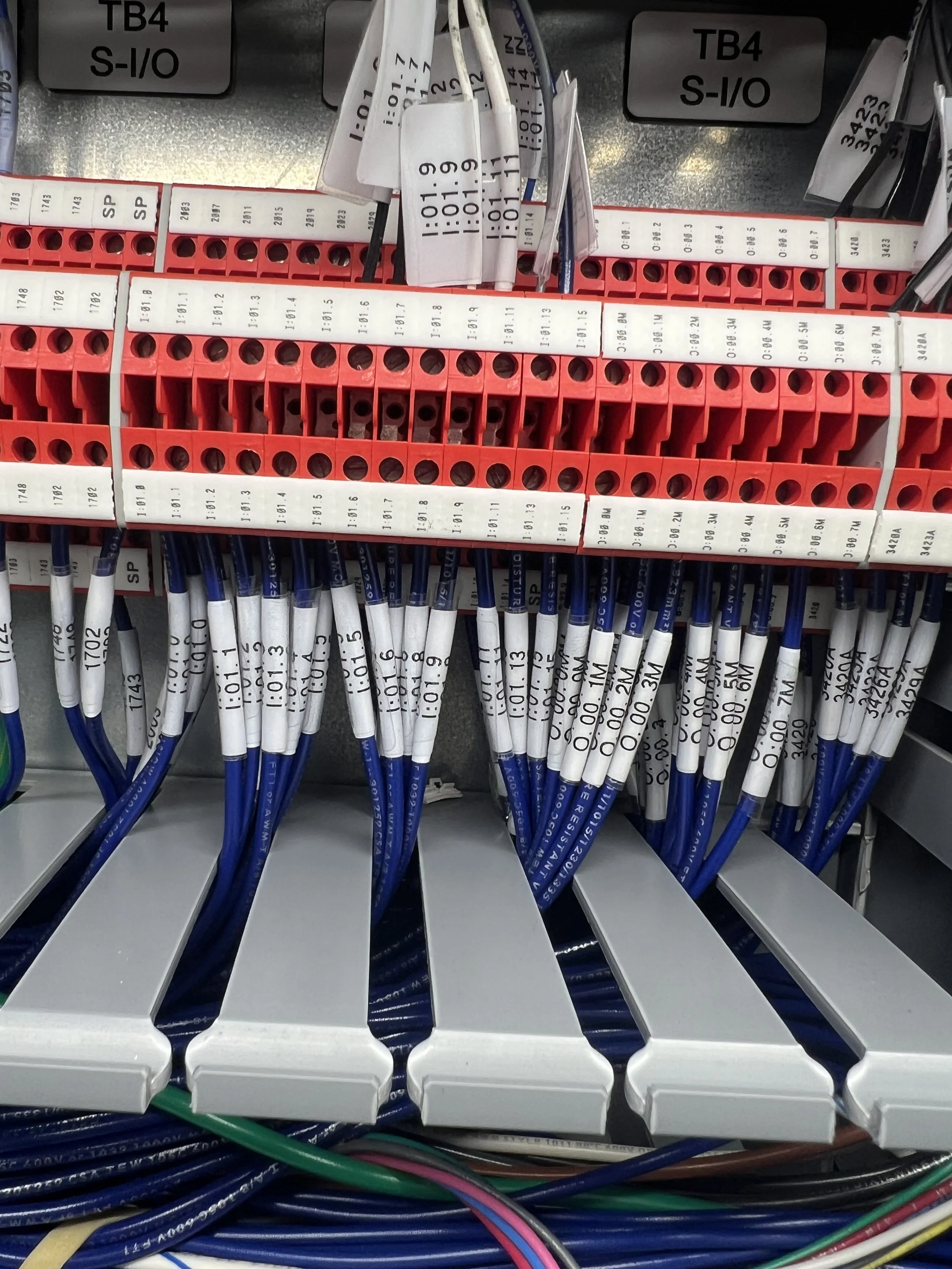 Electrical relay terminal strip with blue wires connected, labeled with various numbers and letters, mounted inside an electrical panel.