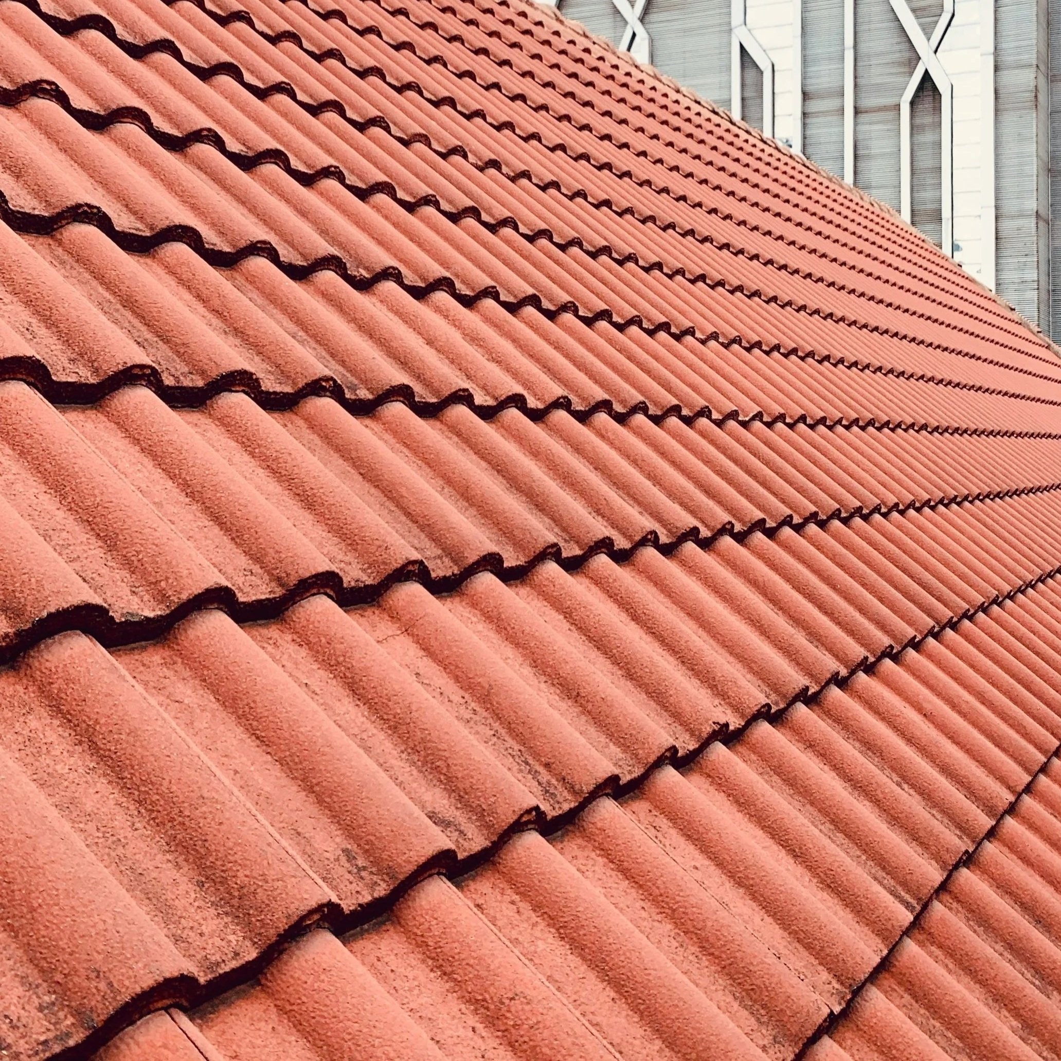 Close-up view of a red clay tiled roof with a modern building in the background.