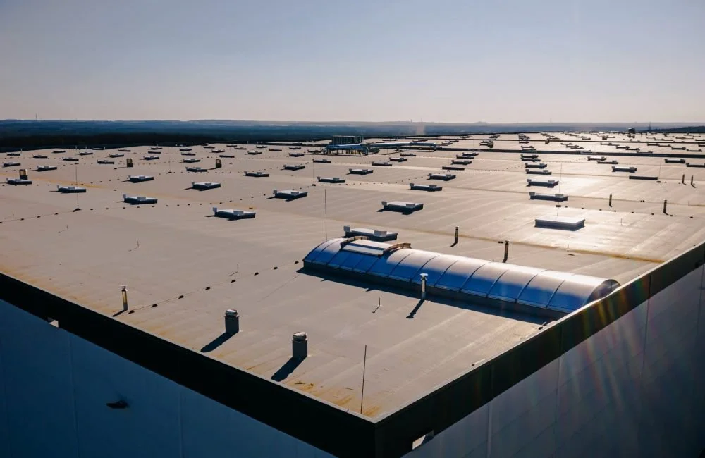 A large industrial building roof with many rooftop HVAC units and a curved skylight, under a clear sky.
