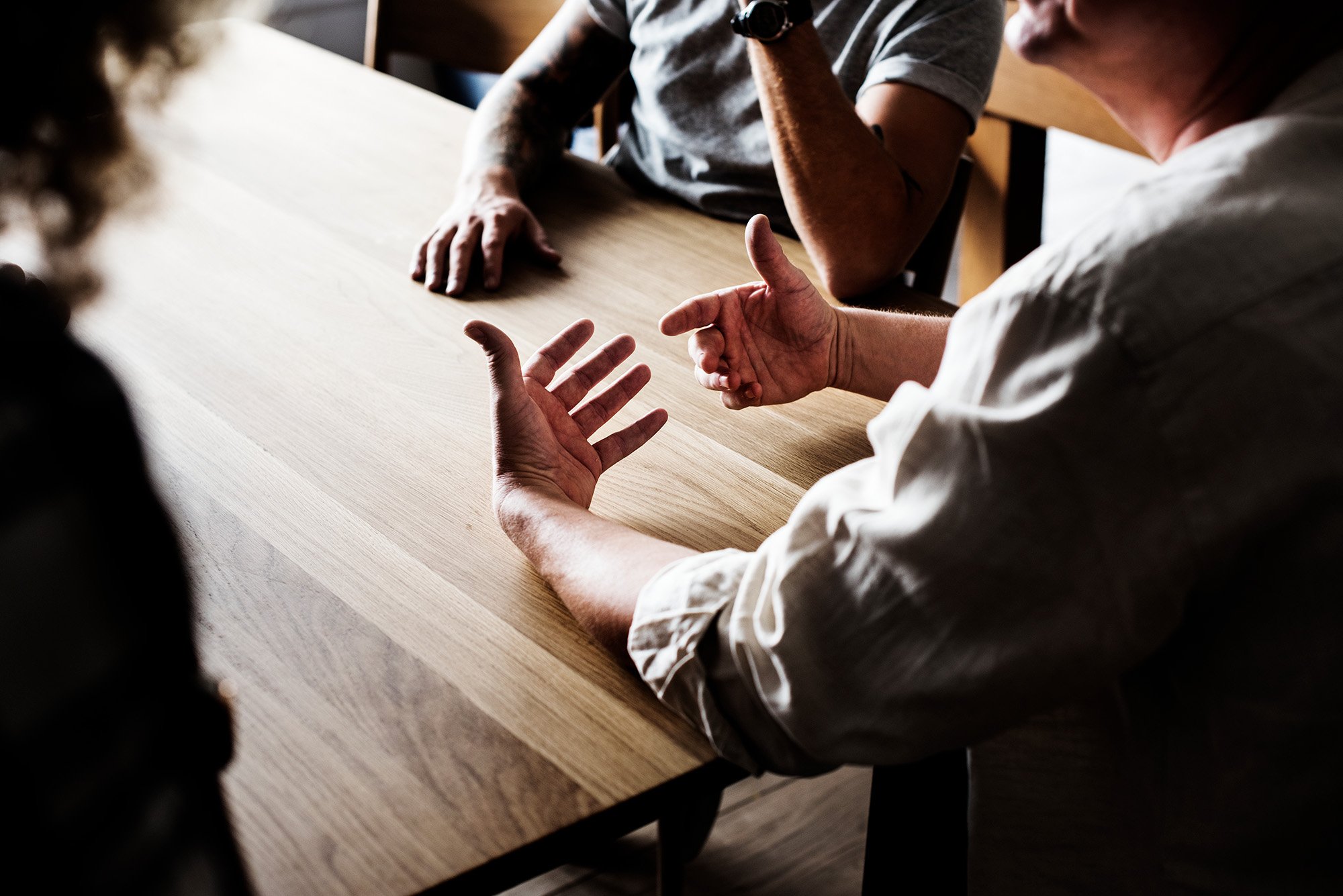 People sitting at a table having a conversation, focusing on their hands and arms.