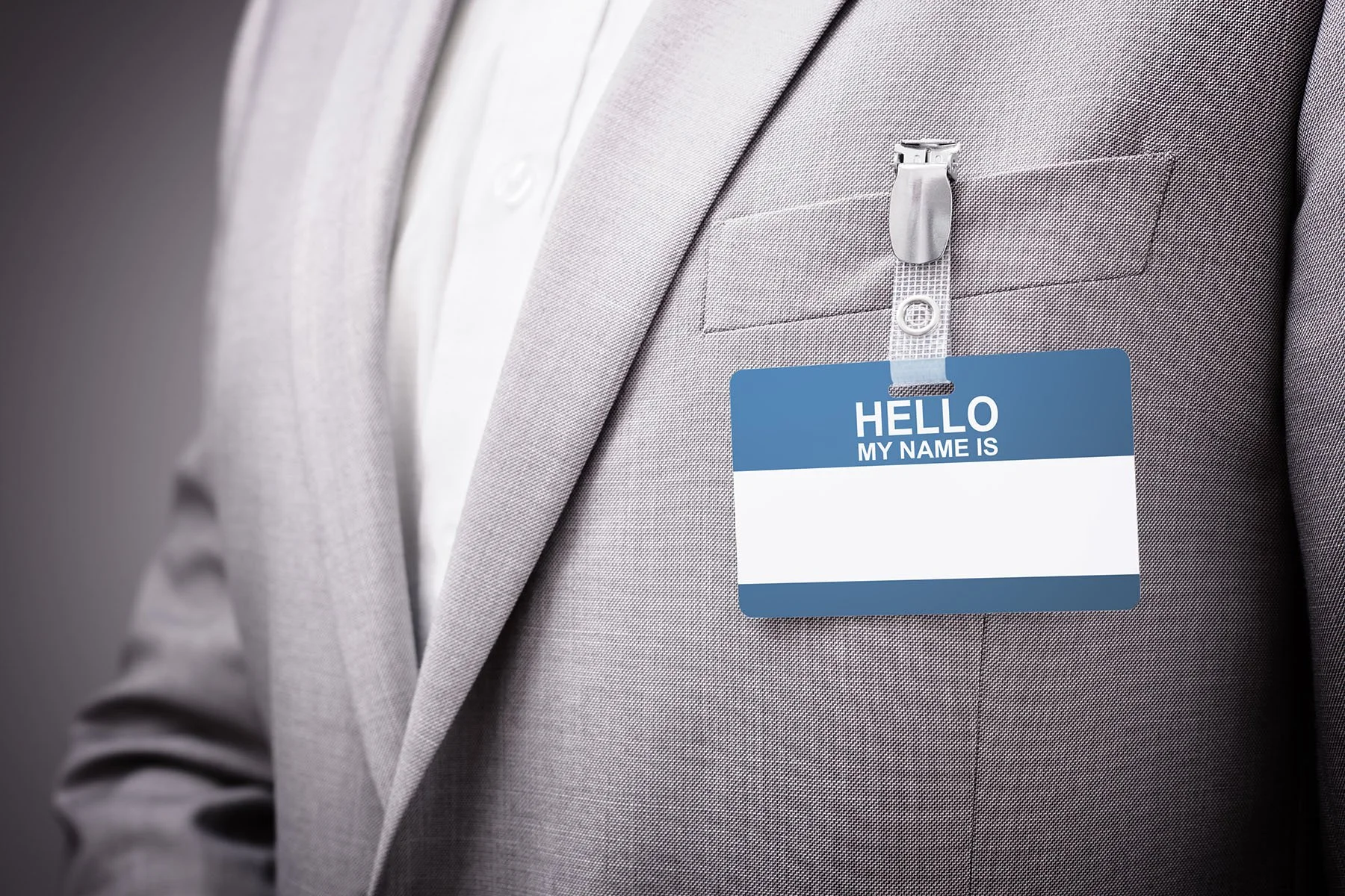 A person wearing a light gray suit with a blue and white identification badge that says "Hello My Name Is".