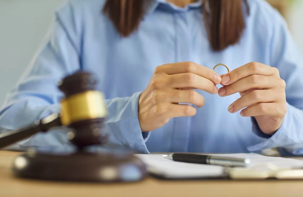 Person in a blue shirt holding a gold wedding ring with a gavel and documents on the table.