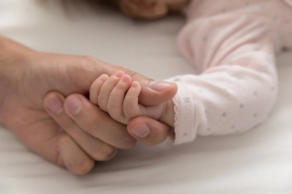 An adult and a child holding hands with their fingers intertwined.