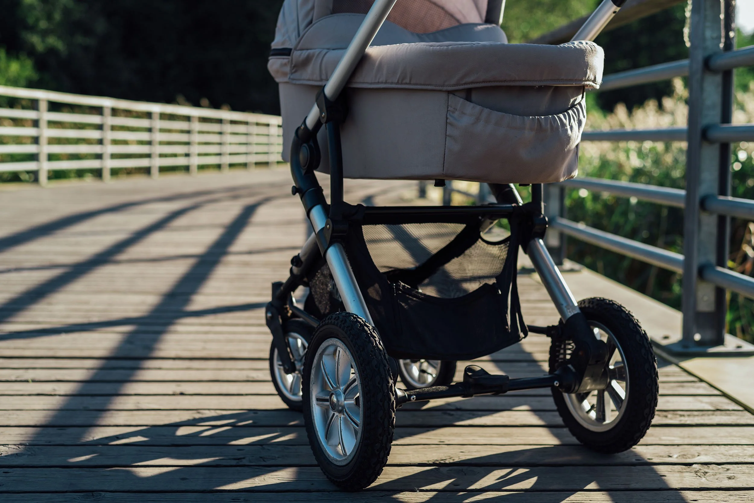 A baby stroller on a wooden walkway with a metal railing, surrounded by greenery.