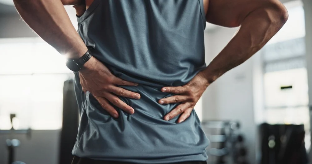 Person holding their lower back in a gym or fitness center.