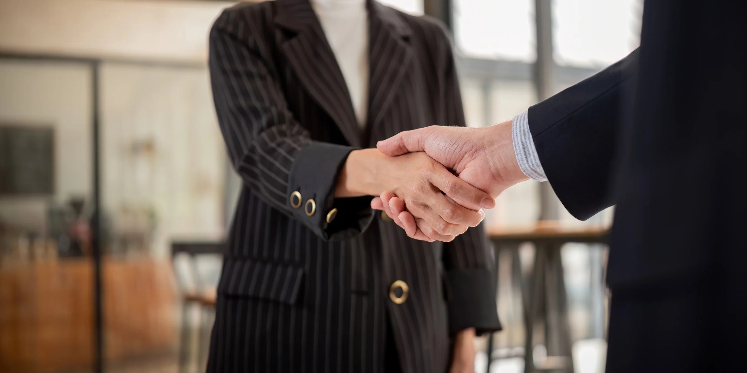 A woman and a man shaking hands in a professional setting.