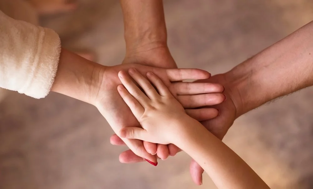 Multiple hands of different sizes and skin tones stacked together in a circle, symbolizing unity and teamwork.