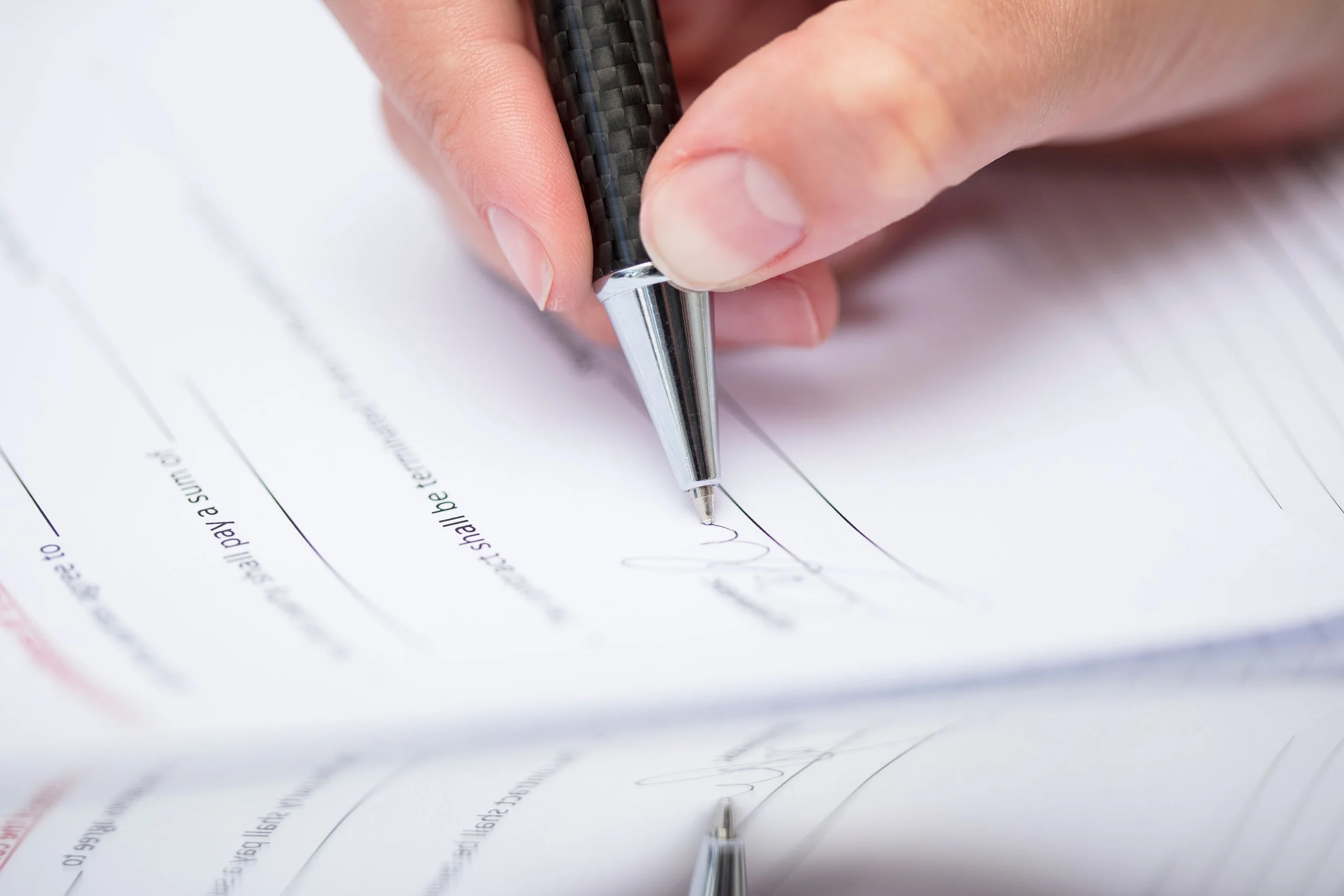 A person signing a document with a black pen on white paper.