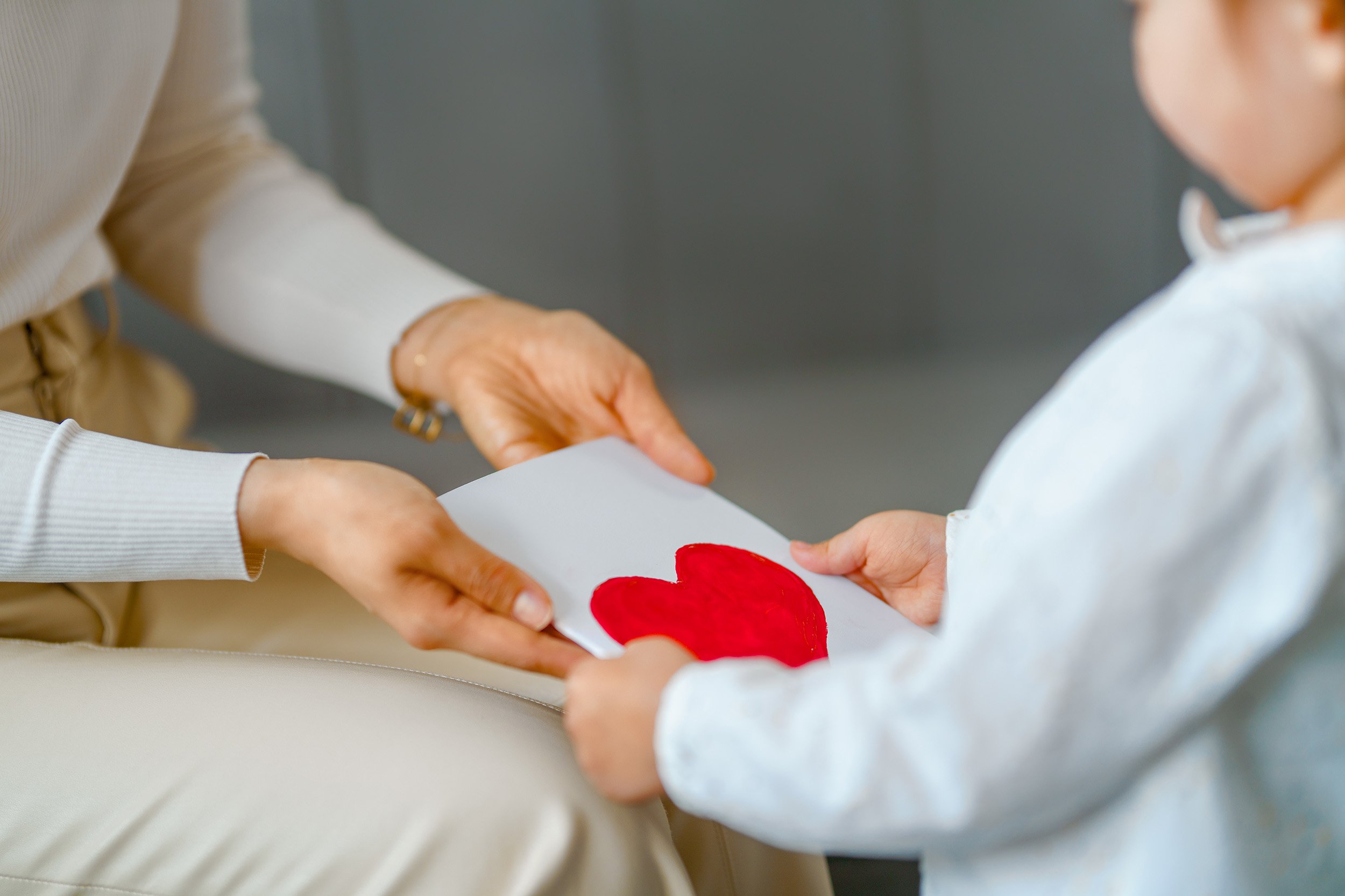 A young child giving a red paper heart to an adult during a Valentine's Day or special occasion gesture.