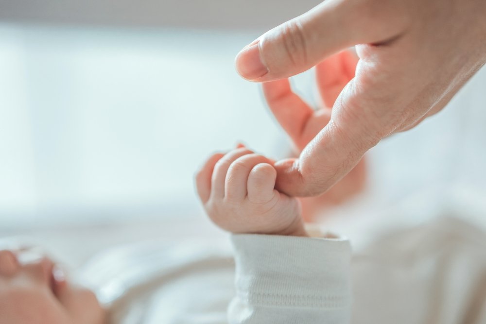 Close-up of a parent's hand gently holding a baby's finger.