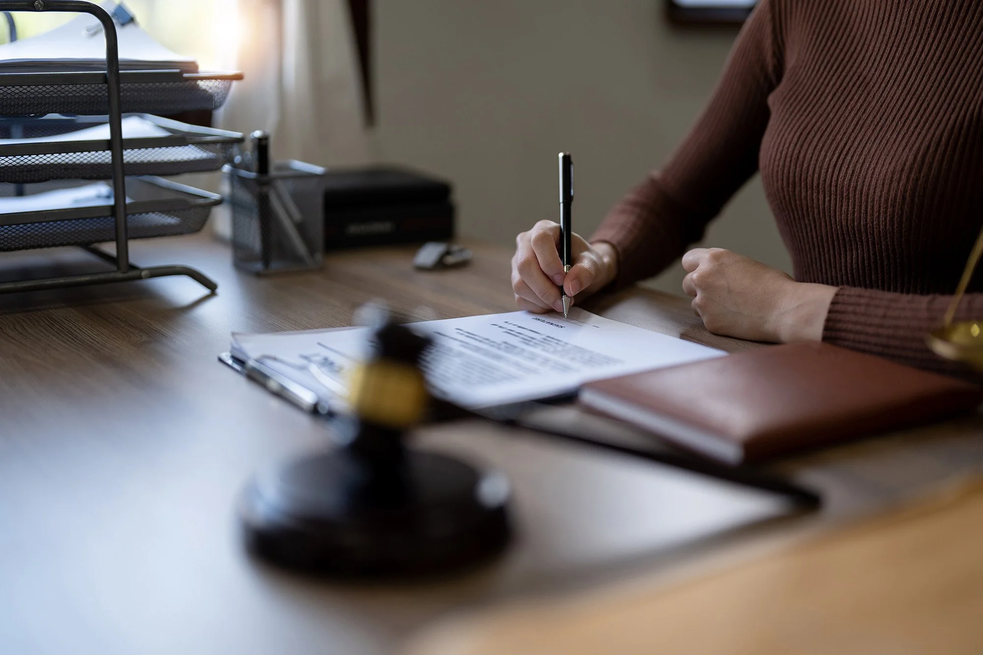 Person writing on a document at a desk with office supplies and organization trays nearby.