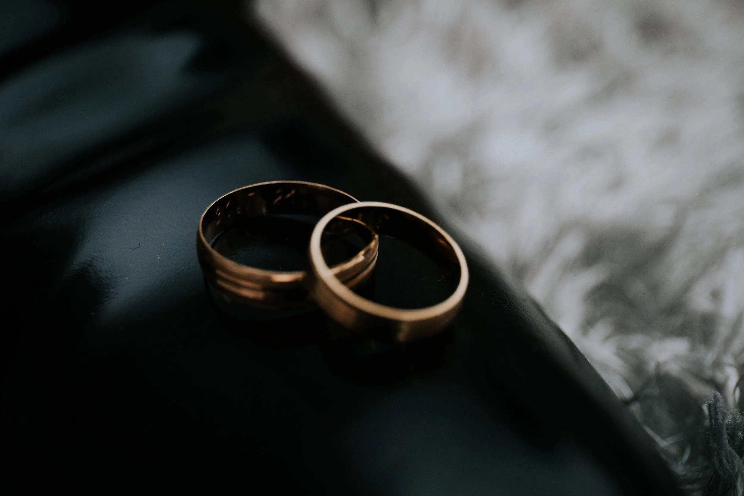 Close-up of two gold wedding rings placed on a dark surface with a blurred background.